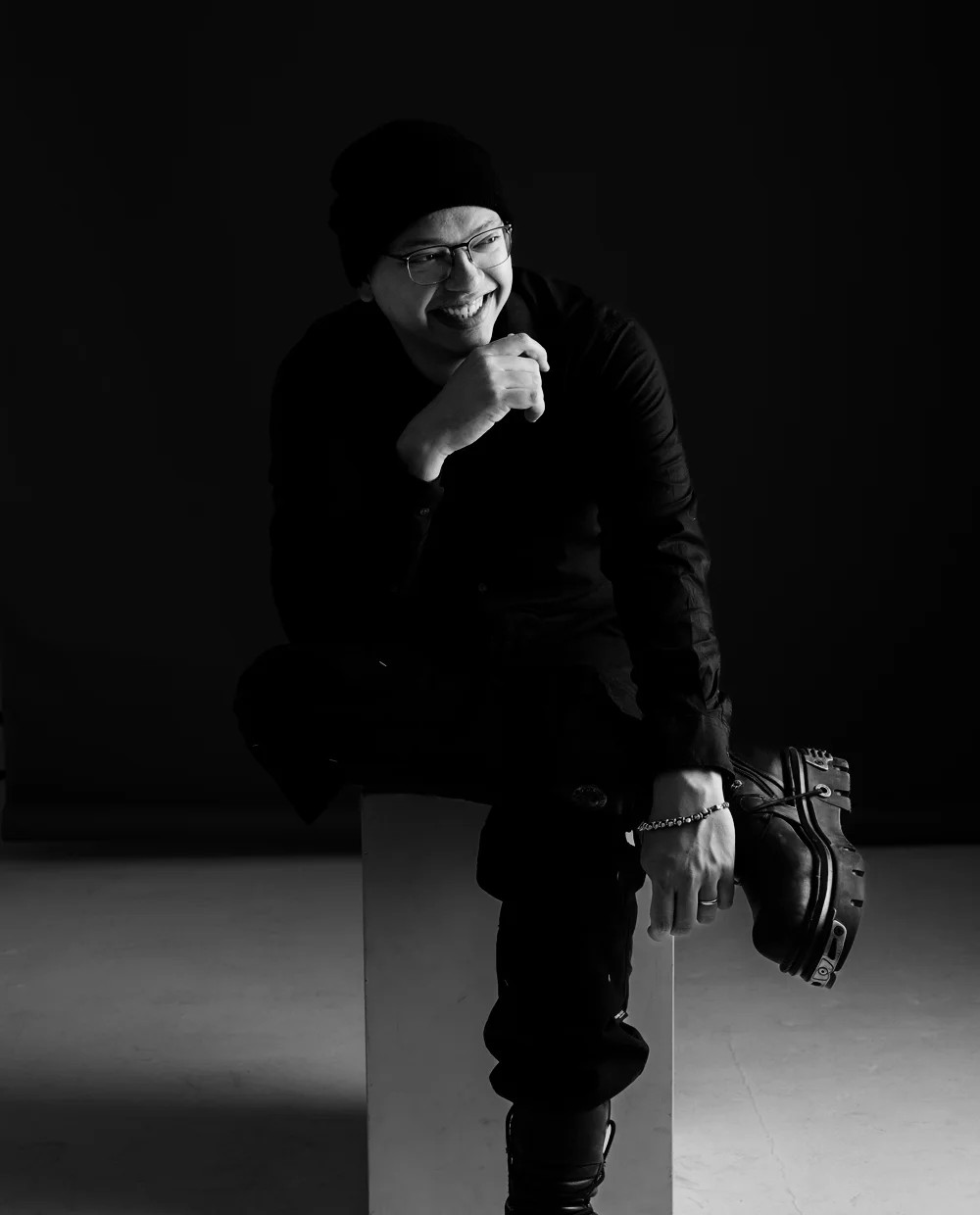 Caio Cesar sentado num banco de estúdio, sorrindo, de gorro e roupa preta
